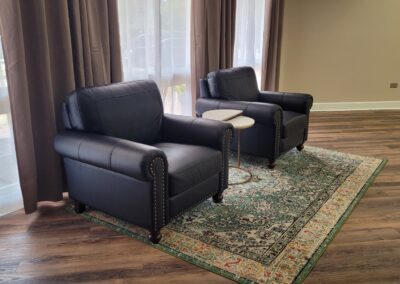 Two black arm chairs in front of a set of windows.